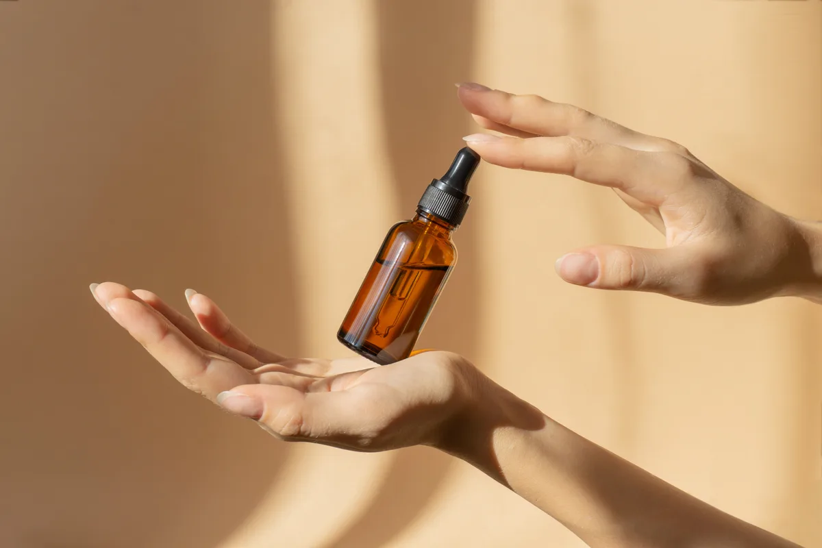 An amber dropper bottle of natural oil held in soft warm light