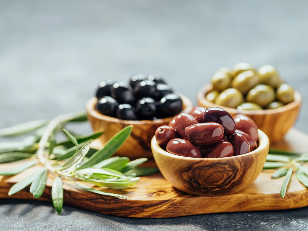 Bowls of green and black olives with jars of brine on a market table