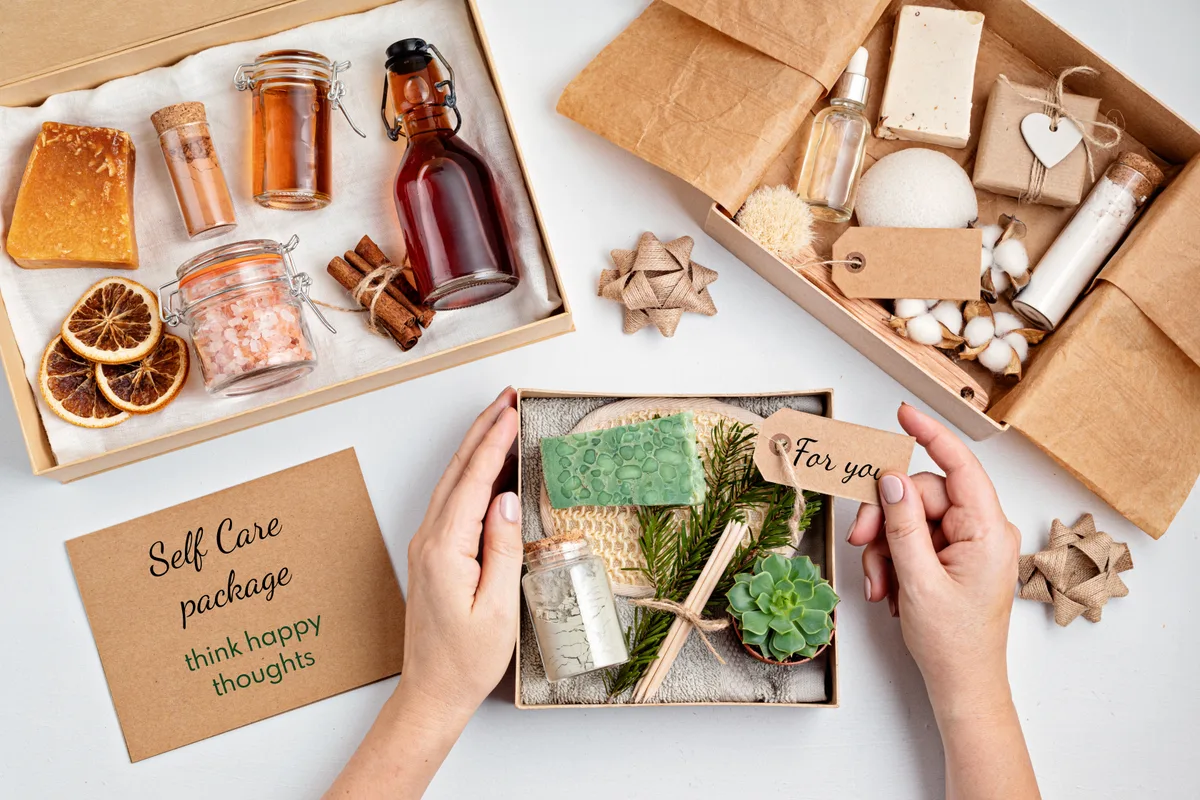 Hands packing a self-care gift box with soap, oils and dried botanicals